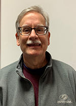 Individual dressed in collared shirt wearing reading glasses, posed for portrait.