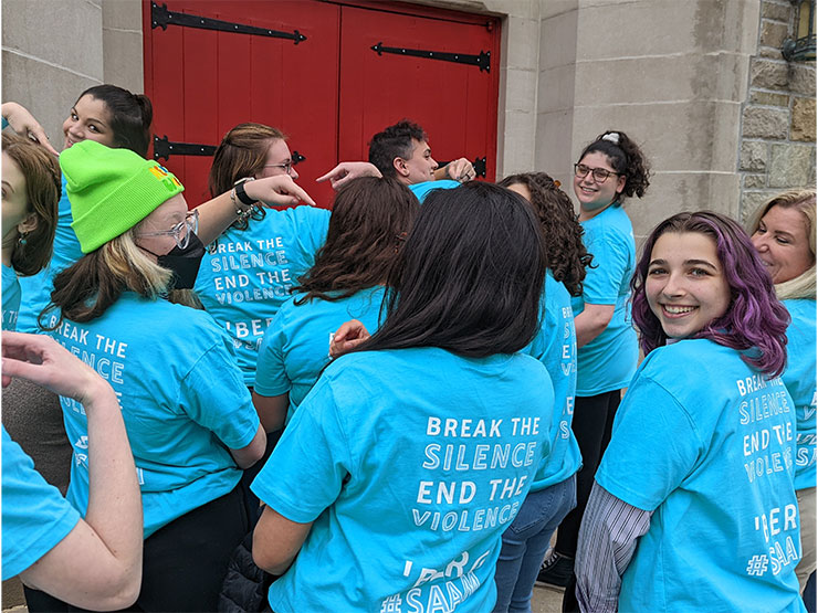 Several young adults pose to model the back of their bright blue t-shirts, which read 