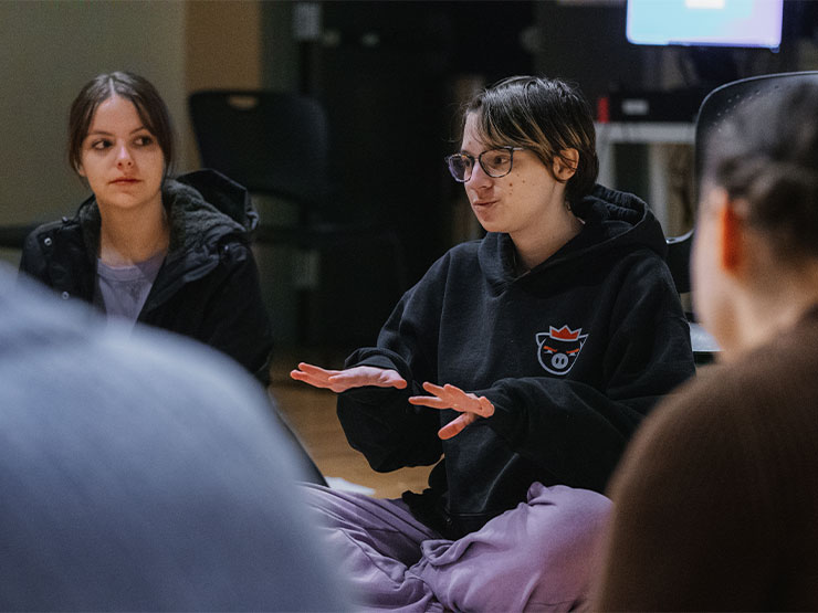 A student, seated in circle, in a studio discusses with the group.