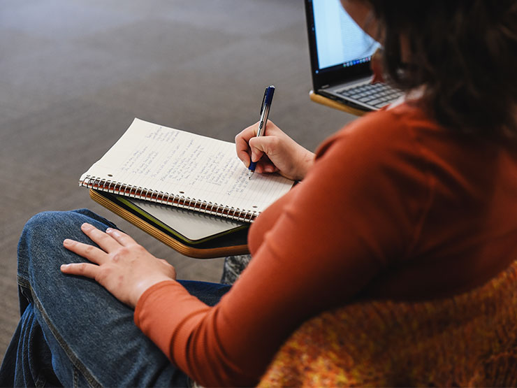 A student seated in a classroom writes in an open notebook.