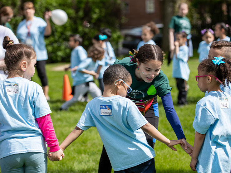 A young adult guides elementary school children in outdoor exercises.