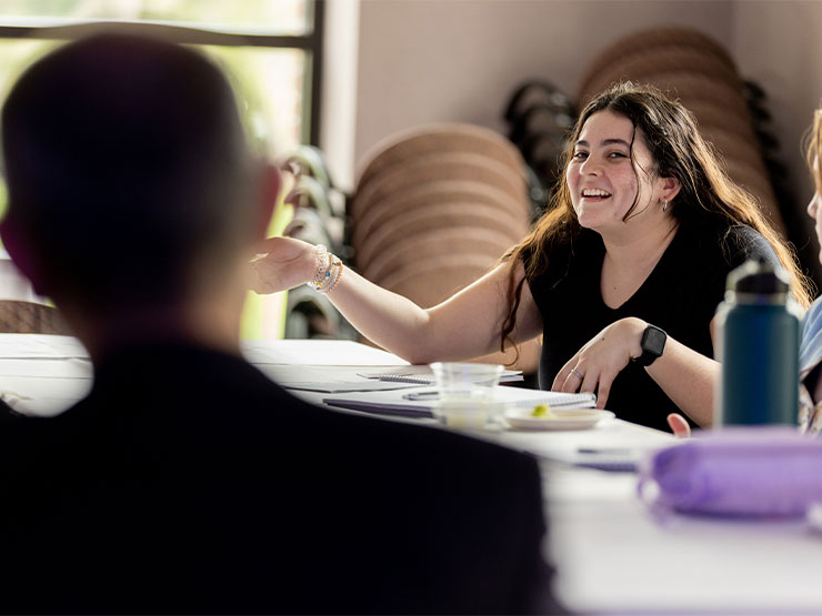 A student smiles wide while speaking to an adult pictured slightly off-camera.