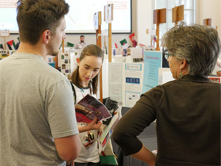 Students and faculty mill around and look through materials at a study abroad fair.