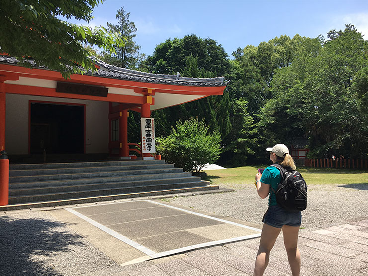 A college student stand outside of a Japanese temple and takes a photograph.