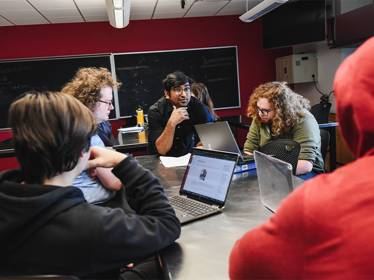 A group of students and an instructor share in a discussion around a table in a classroom.