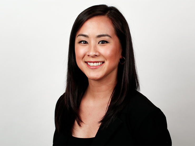 A headshot of a media professional with long dark hair, wearing a dark blouse and blazer.