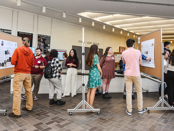 College students mingle with faculty, staff, students and others around poster boards depicting details student research projects.