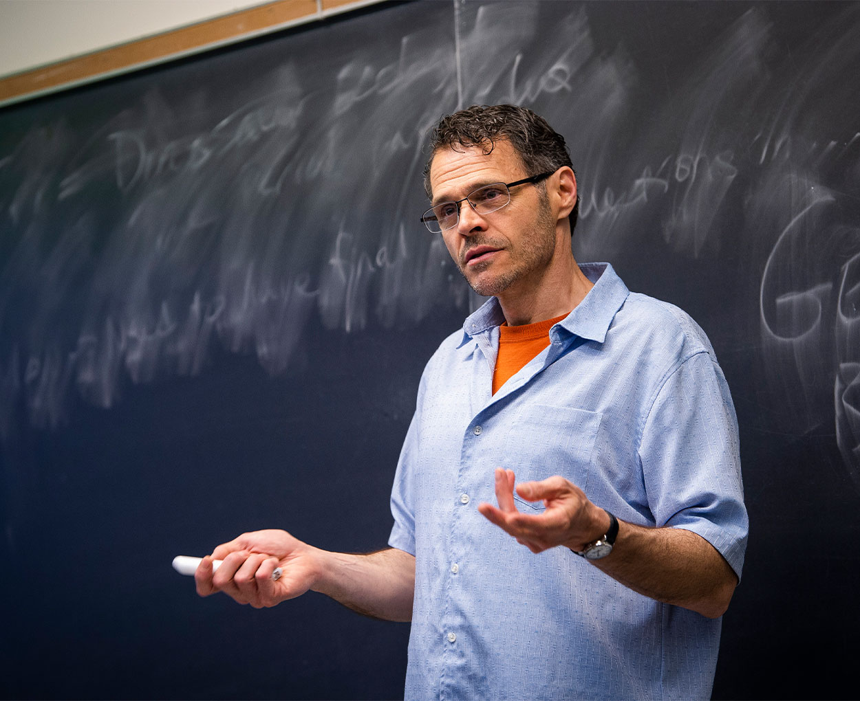 A male instructor speaks in front of a chalkboard.