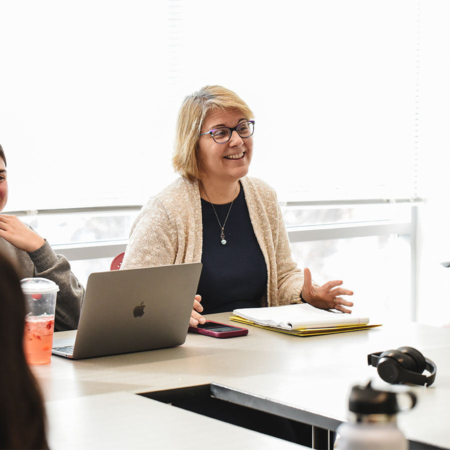 A college professor in glasses smiles while teaching a class.