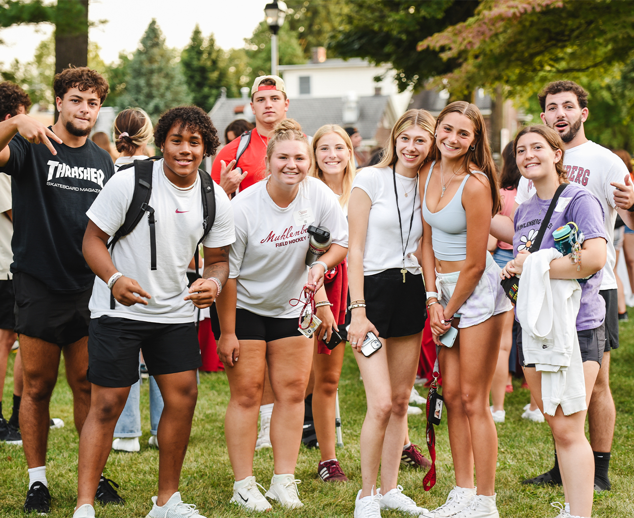 A group of nine smiling students pose on a college green for a photo.