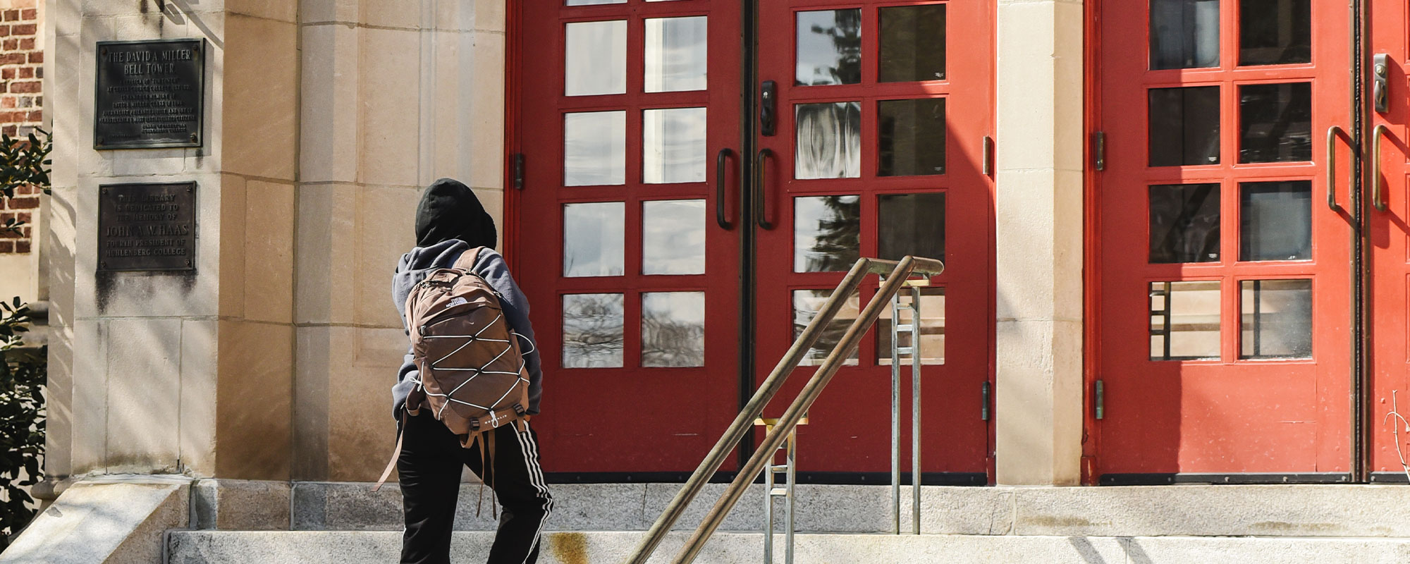 A student walks toward a pair of red doors on a college campus.