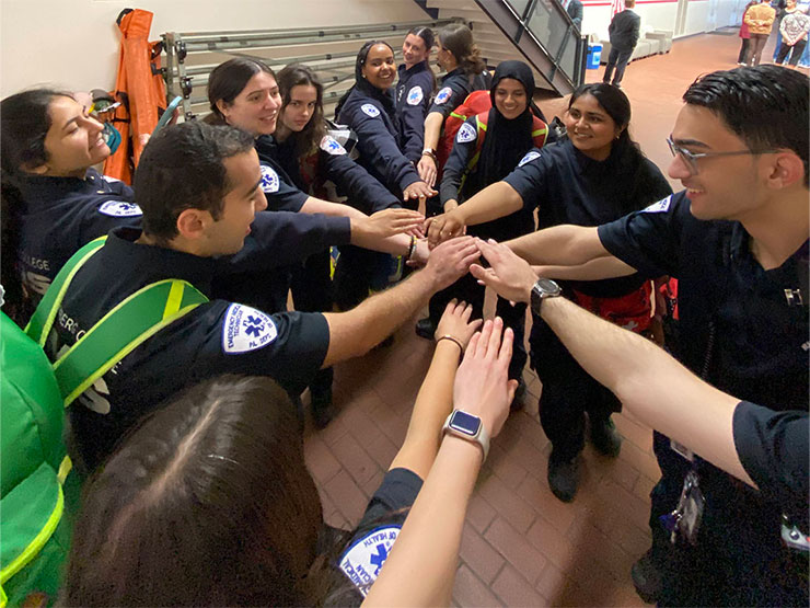 A group of college students in EMS uniforms put their hands into the middle of a circle