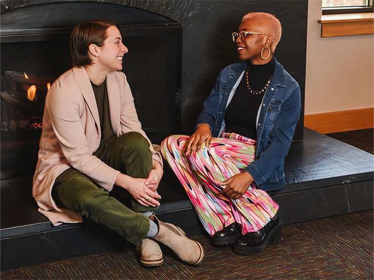 A college librarian and a college student sit by a fireplace and talk.