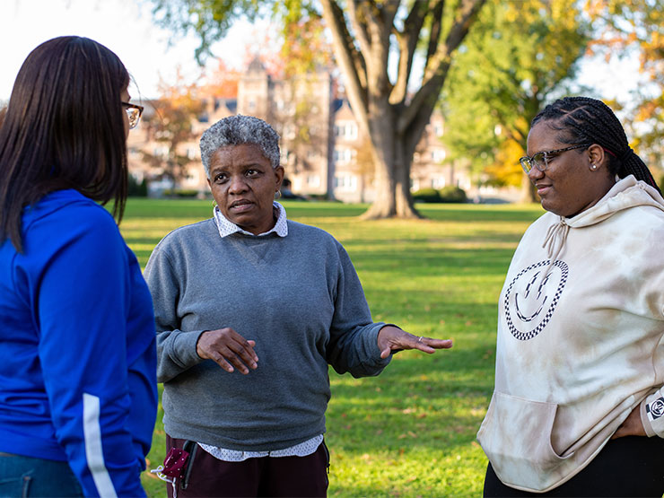 A college staff member holds a conversation with two students outdoors.