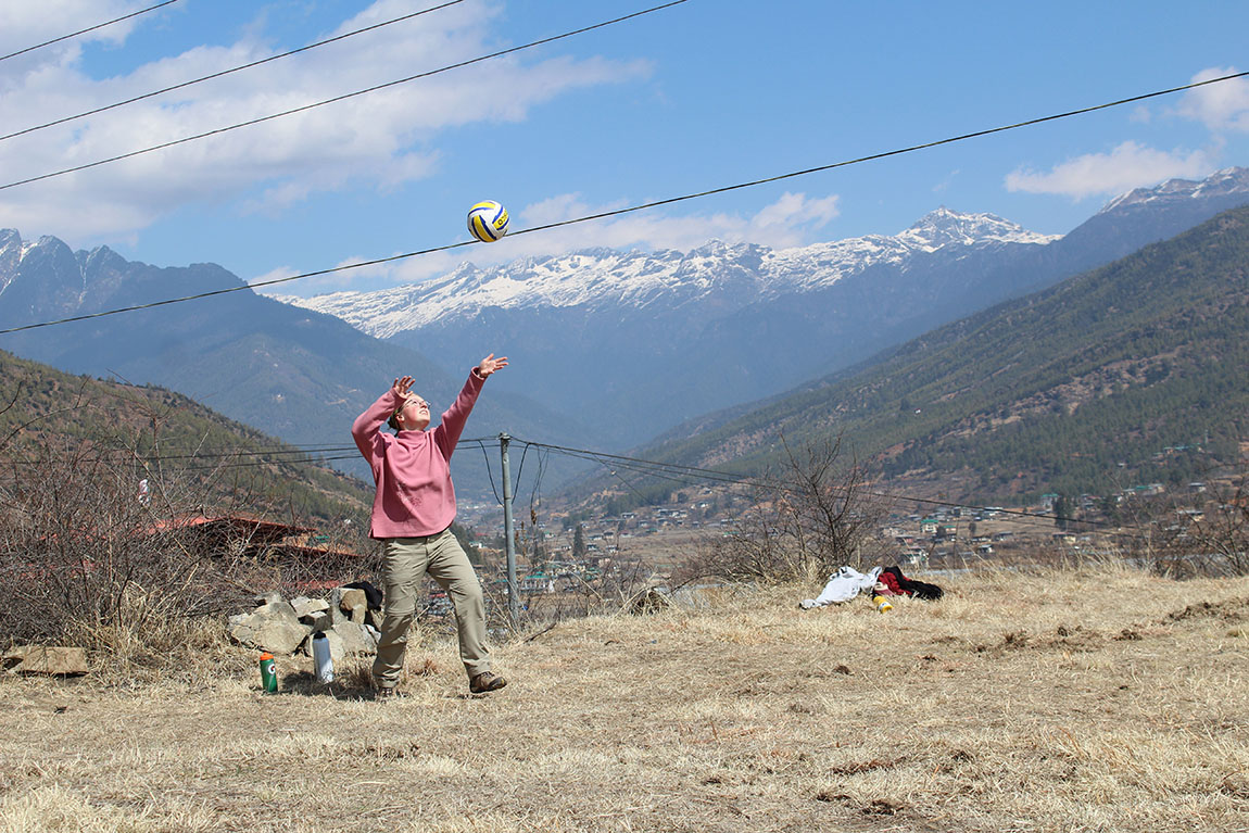 A college student throws a volleyball in the air with snow-capped mountains in the background