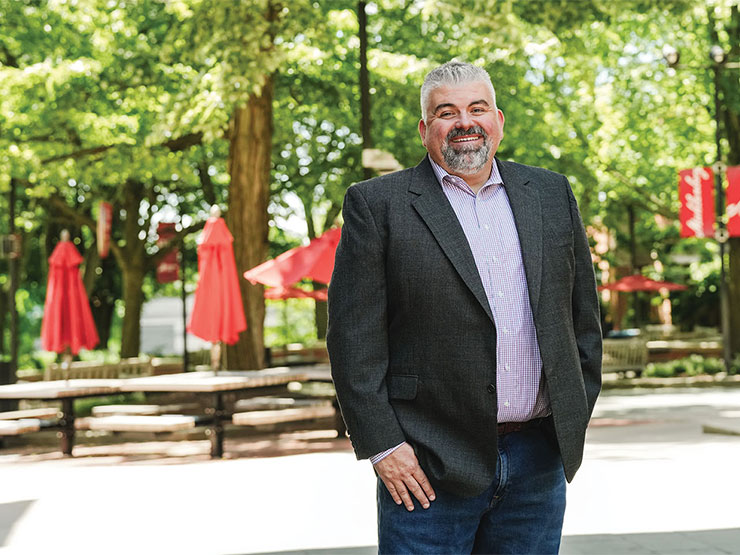 A man in a suit smiles for a photo outside on a college campus.