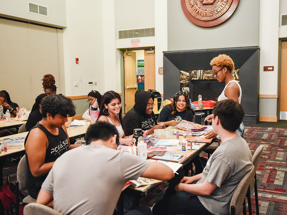 A group of college students gather around a table to make collages