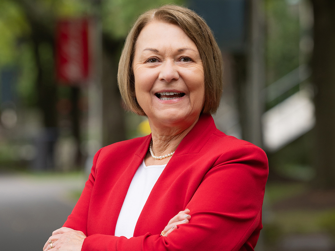 A college president in a red blazer smiles for a headshot outside on campus