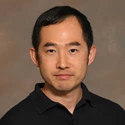 A headshot of a college professor with short dark hair and a black shirt on