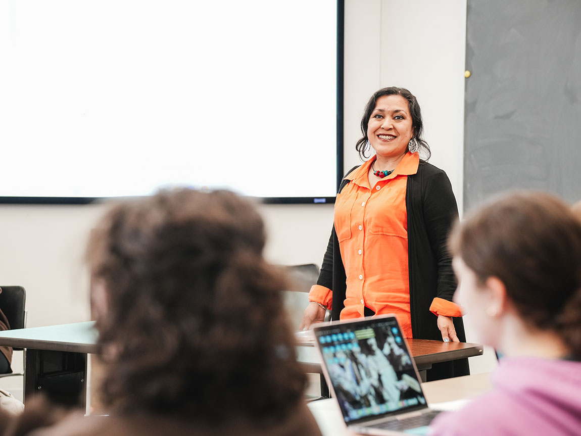 A college professor in an orange shirt speaks to her class