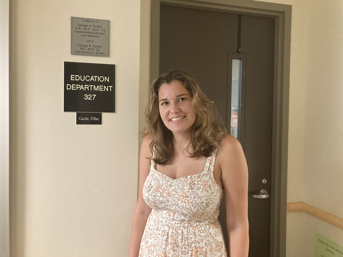 A college student smiles for a photo in front of a sign that says education department