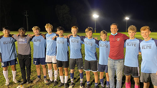 An adult in a red shirt poses with several teenage athletes in light blue jerseys.