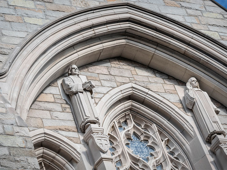 Robed figures holding books are carved into the stone in the front of a chapel.